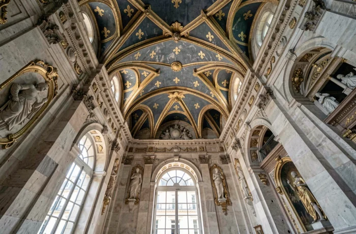 Vue grand angle de l'intérieur d'une salle de palais royal français avec motifs de fleurs de lys sculptés dorés et bleus sur les moulures et plafonds peints
